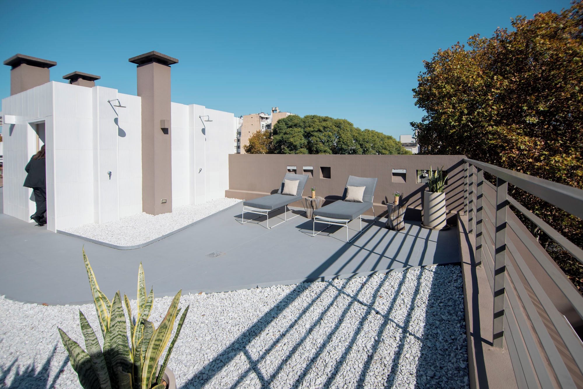 A rooftop terrace with sun loungers, a wooden deck, and a white gravel area.
