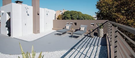 A rooftop terrace with sun loungers, a wooden deck, and a white gravel area.