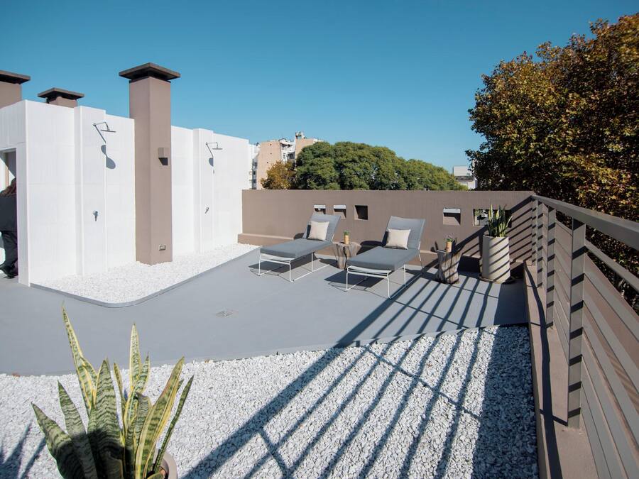 A rooftop terrace with sun loungers, a wooden deck, and a white gravel area.