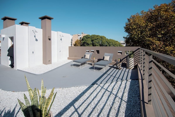 Une terrasse sur le toit avec des chaises longues, une plateforme en bois et un espace recouvert de gravier blanc.
