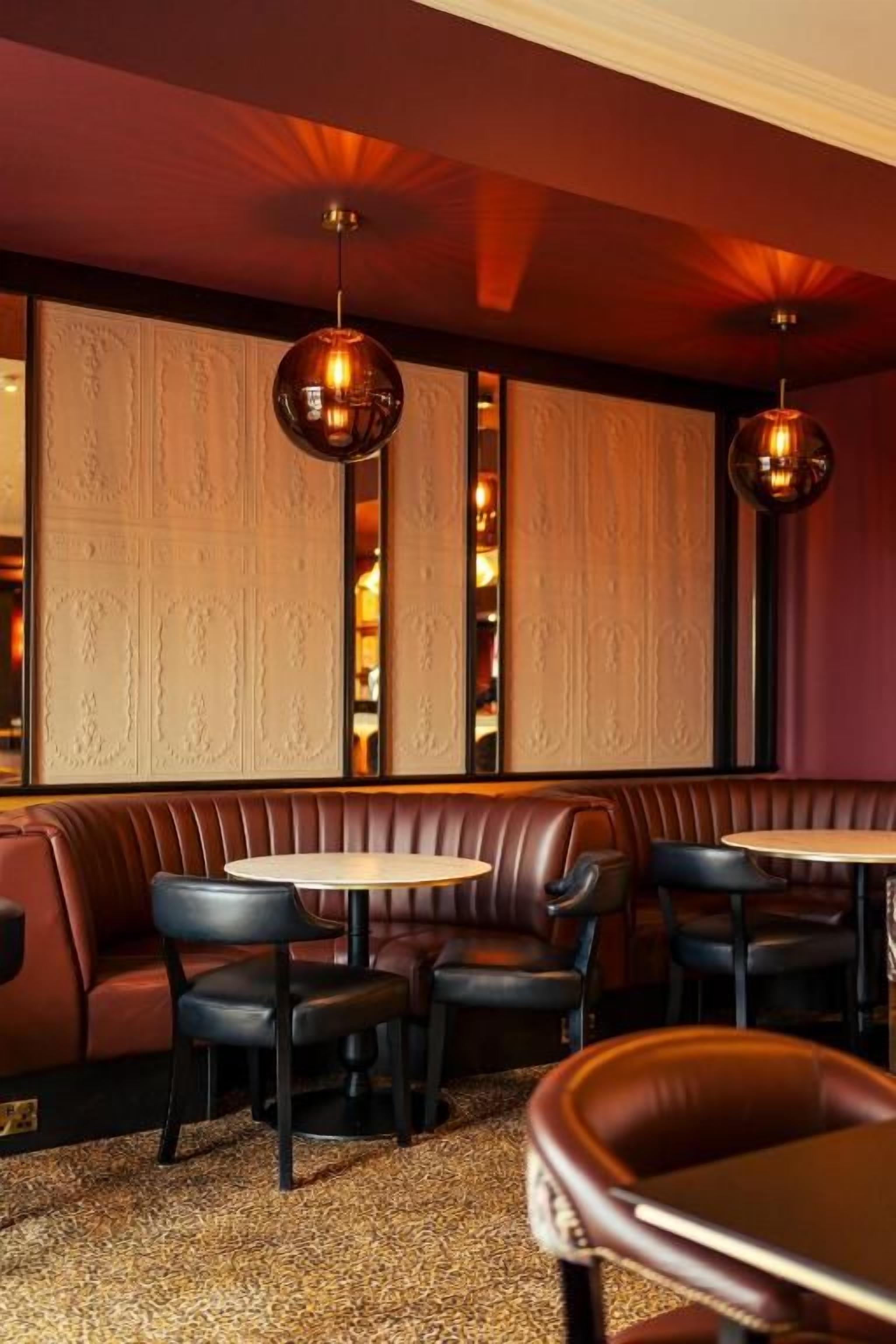 L’intérieur d’un restaurant avec des banquettes, des tables rondes et des luminaires suspendus.