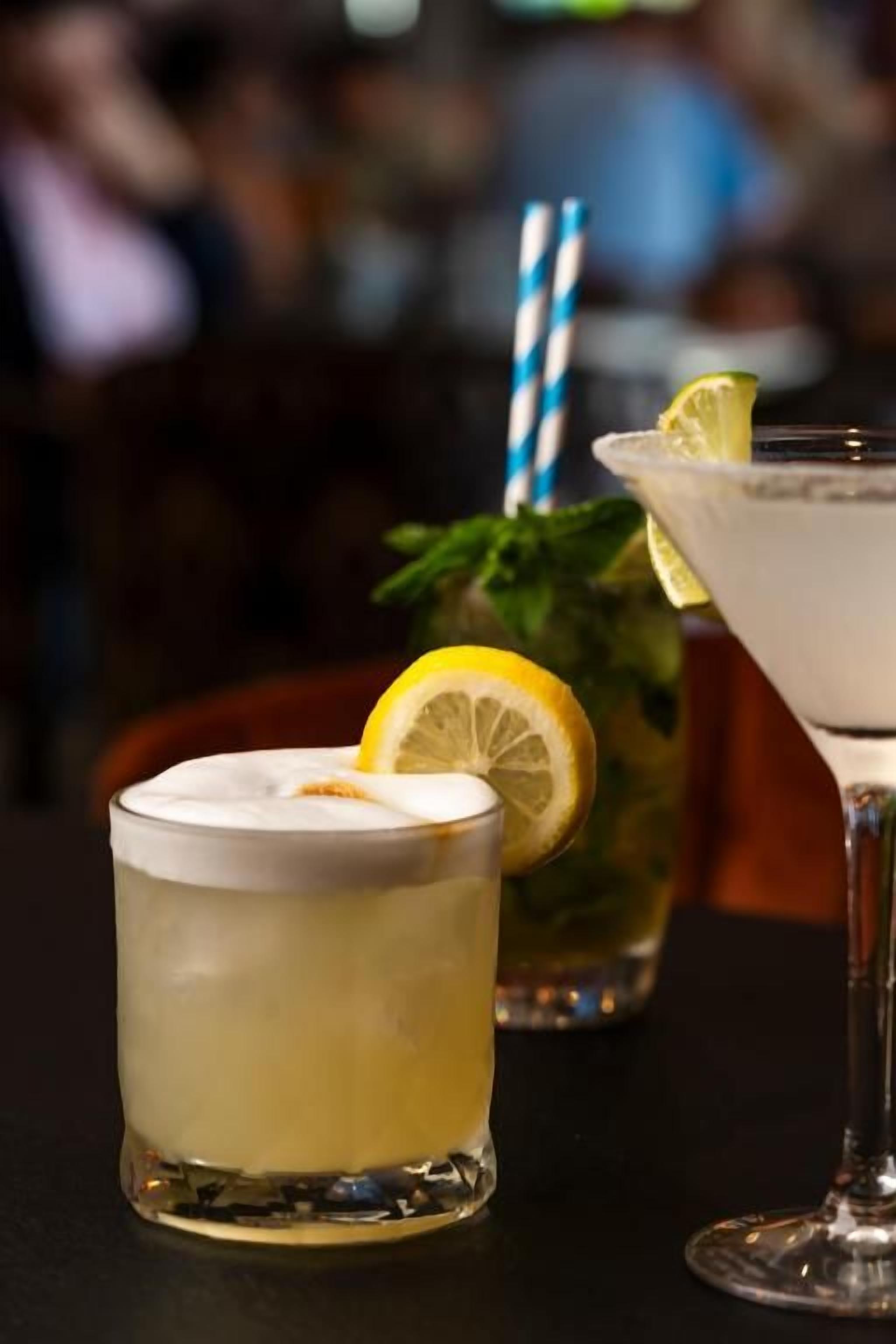Three drinks on a table, one with a lemon wedge and a blue and white striped straw.