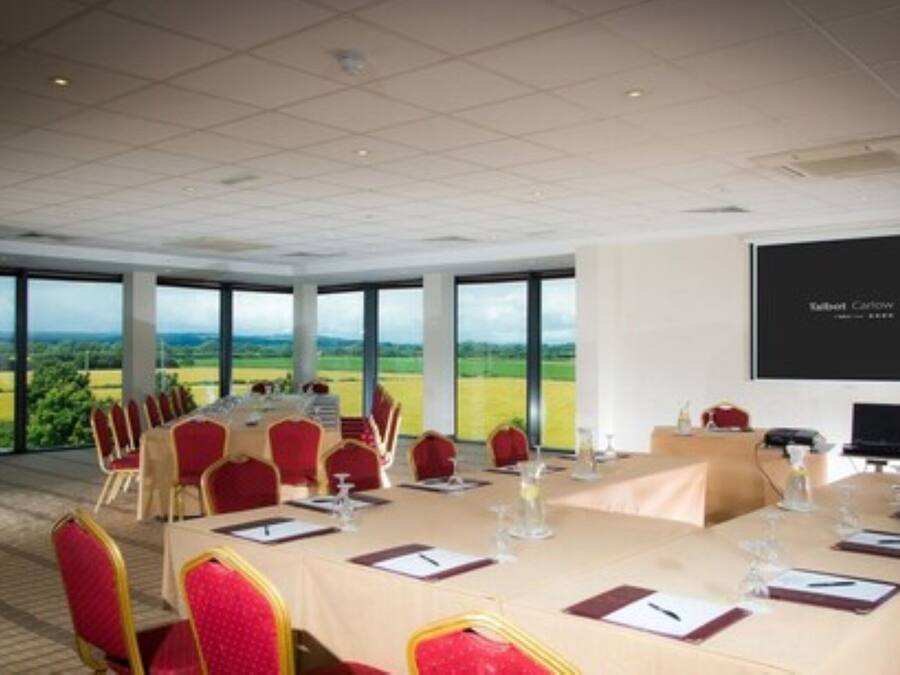 A conference room with a large table, red chairs, and a projector screen displaying "Talbot Carrow".