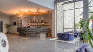 A modern reception area with a tufted black reception desk, a large window with a stone wall, and a seating area with blue sofas. - Talbot Hotel Carlow (Carlow)