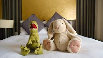 A bed with two plush toys, a green dinosaur and a white rabbit, in a room with a yellow headboard and striped wallpaper.