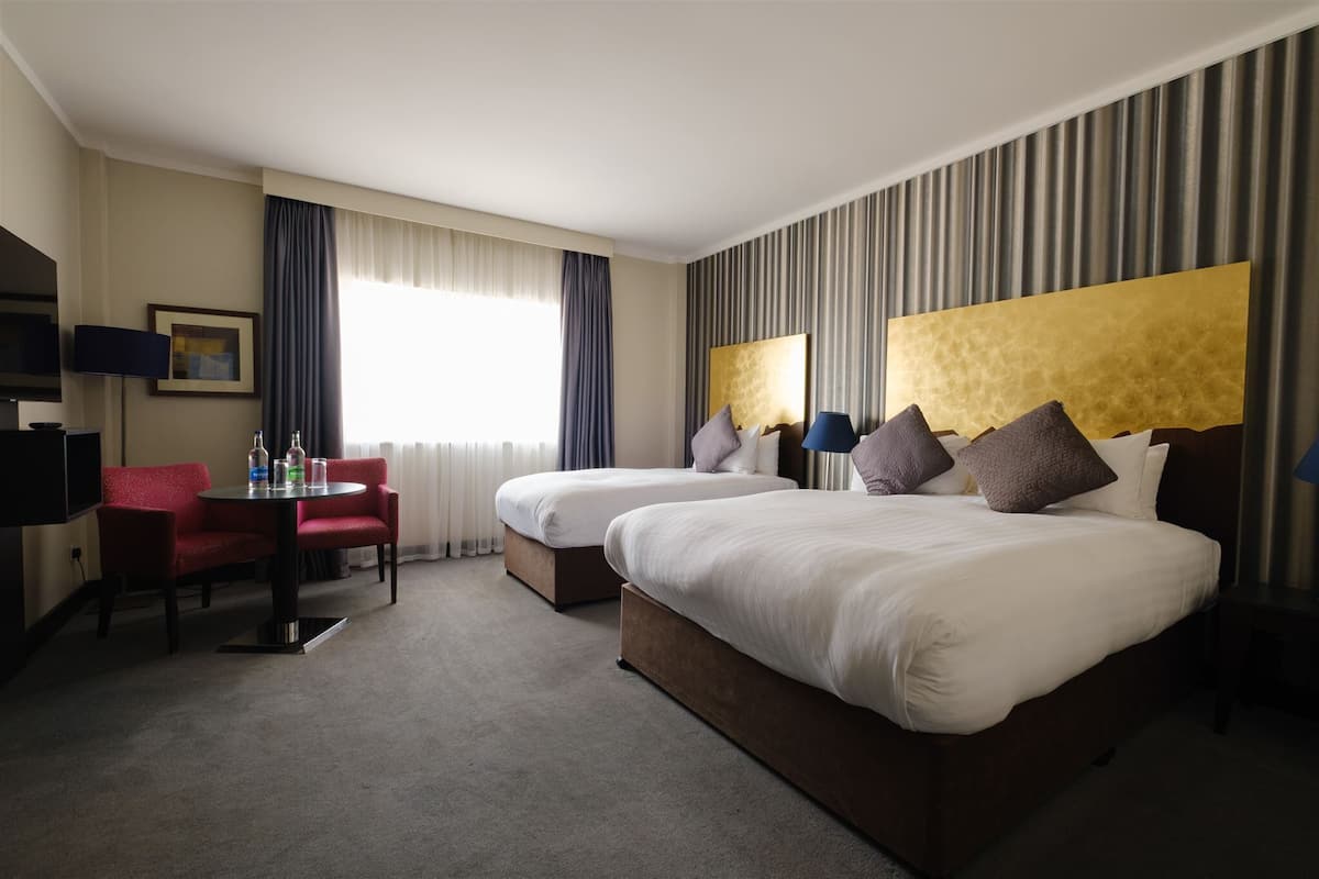 A hotel room with two beds, a desk, a chair, and a TV.