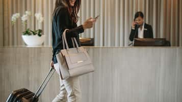 A person with a suitcase and a handbag walking past a reception desk in a hotel lobby.
