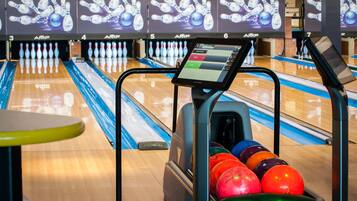 A bowling alley with lanes numbered 3 to 7, a bowling ball return machine, and a bowling ball rack filled with colorful balls.