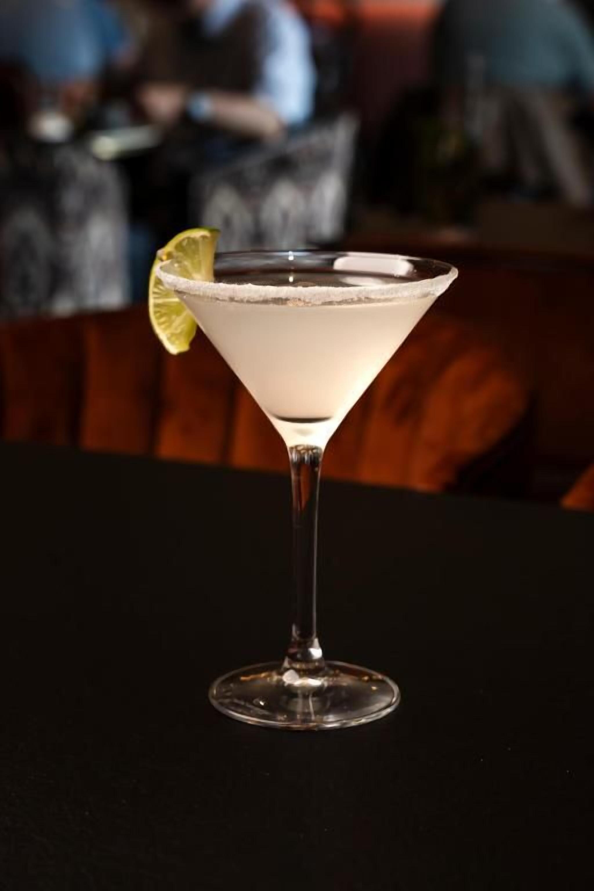 Una copa de martini con una rodaja de lima sobre una mesa negra en un bar.