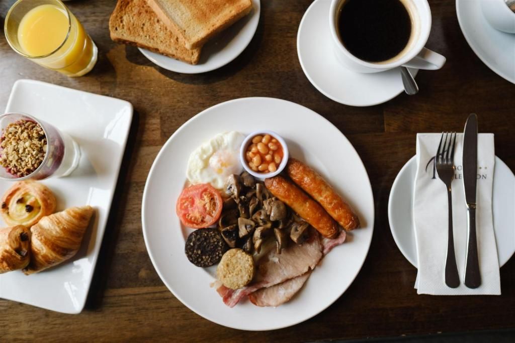 A breakfast setting with toast, eggs, sausages, mushrooms, and beans on a plate, accompanied by a glass of orange juice and a cup of coffee.