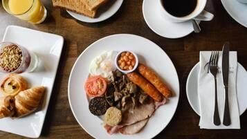 A breakfast setting with toast, eggs, sausages, mushrooms, and beans on a plate, accompanied by a glass of orange juice and a cup of coffee.