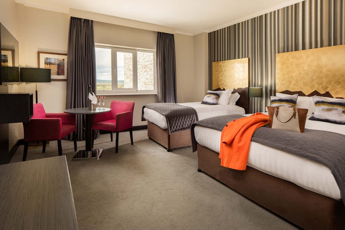 A hotel room with two beds, a desk, a chair, and a window with curtains.