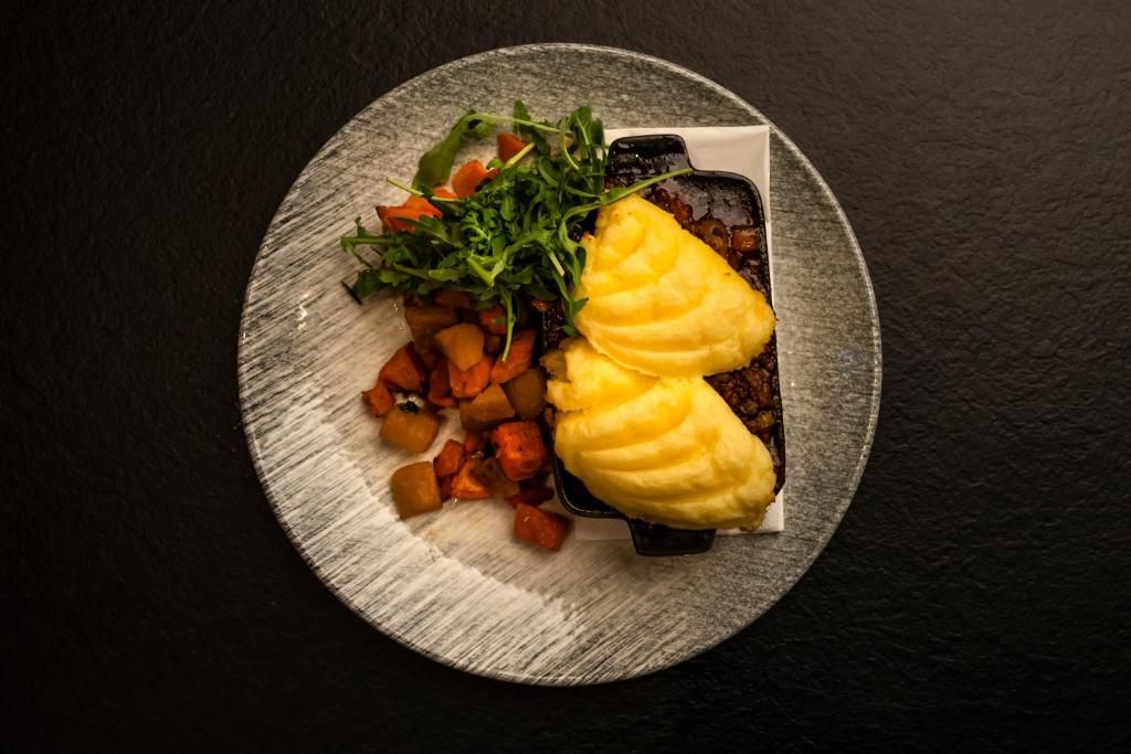 Een bord met aardappelpuree, geroosterde groenten en een salade op een bord met een structuur.