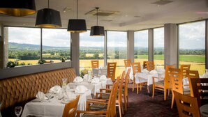 A restaurant with a view of the countryside, featuring tables set with white tablecloths and wooden chairs. - Talbot Hotel Carlow (Carlow)