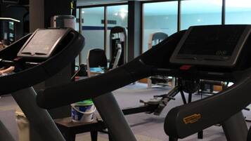 Una palestra con tapis roulant e attrezzature per esercizi, ampie finestre e vista sul cielo.