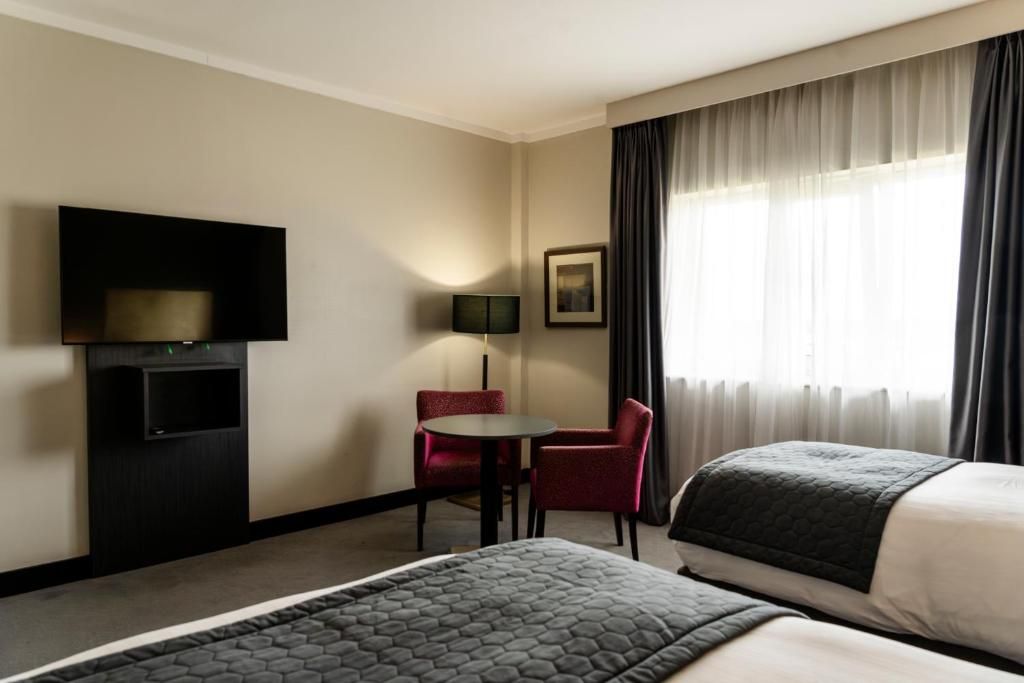 Et hotelværelse med to senge, fjernsyn, skrivebord og stol.