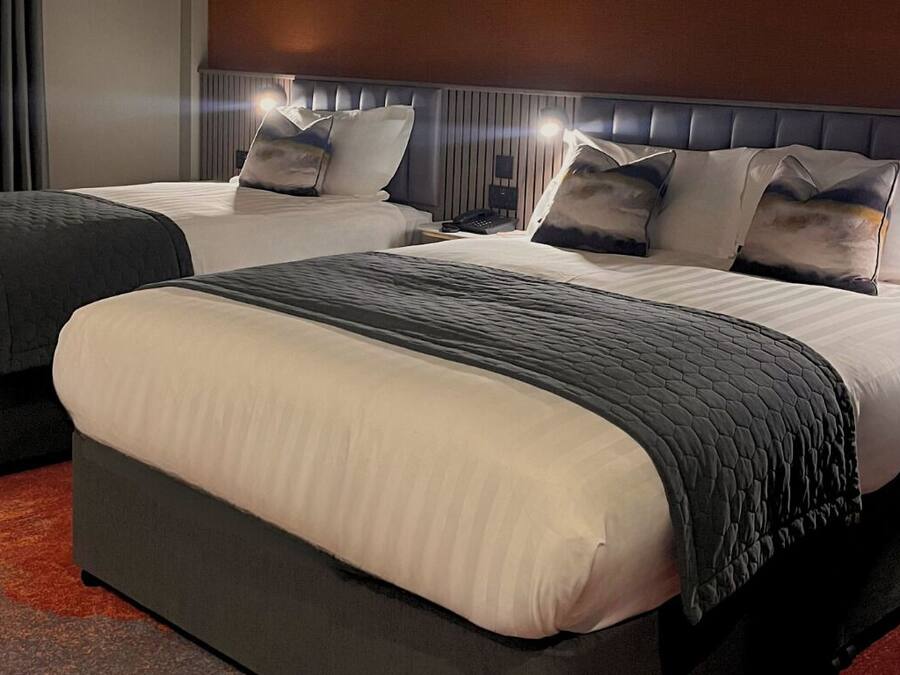 Habitación de hotel con dos camas, cada una con cabecero, mesita de noche y lámpara.