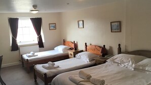 A hotel room with two single beds, a wooden headboard, a bedside table with a lamp, and a window with curtains. - White Hart Hotel (Martock)