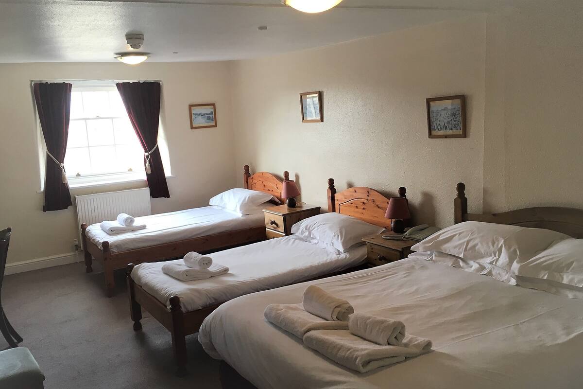 A hotel room with two single beds, a wooden headboard, a bedside table with a lamp, and a window with curtains.