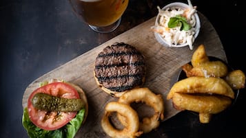 A meal with a grilled burger, onion rings, and a side salad on a wooden board.