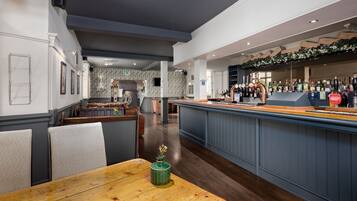 A restaurant with a bar area, wooden tables, and chairs.