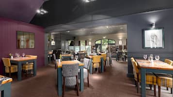 Un restaurant doté de nombreuses tables et chaises, d’un tapis à motifs et d’œuvres d’art encadrées accrochées aux murs.
