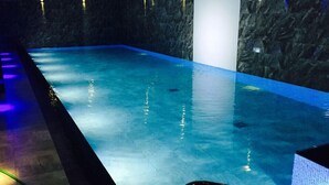 Piscina interna com parede escura e texturizada e águas azuis transparentes.