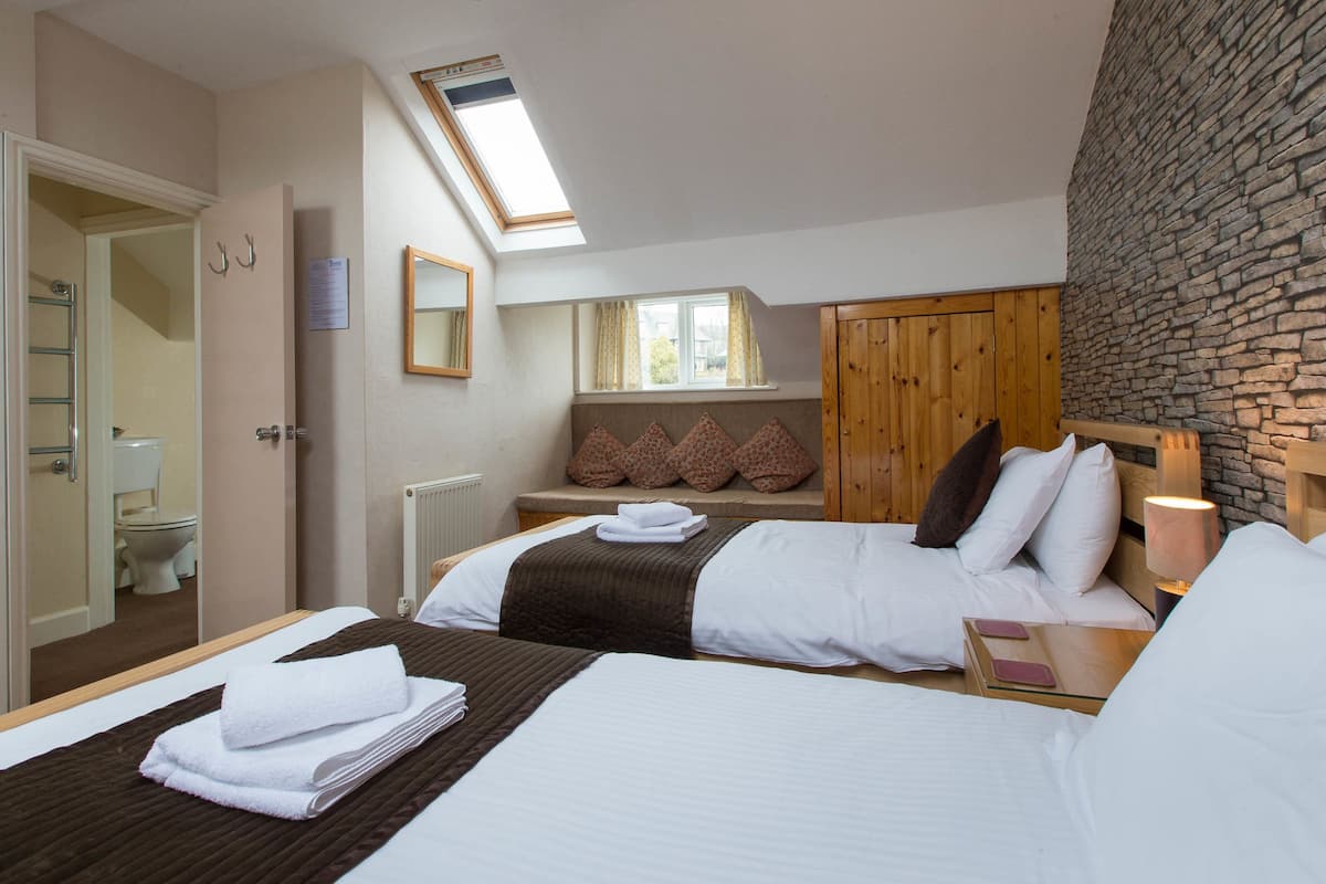 A hotel room with two beds, a skylight, a stone wall, and a view of the outside.