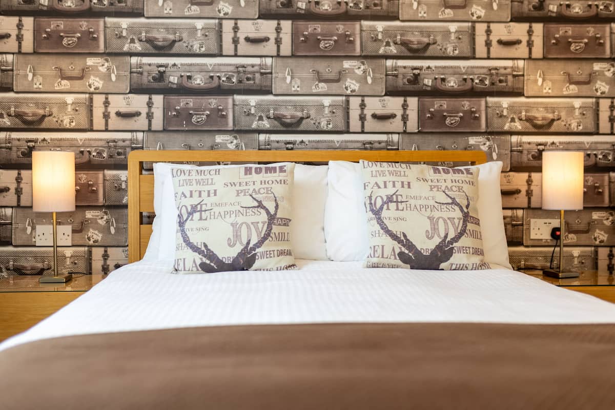 A hotel room with a bed, pillows with motivational phrases, and a wall decorated with vintage suitcases.