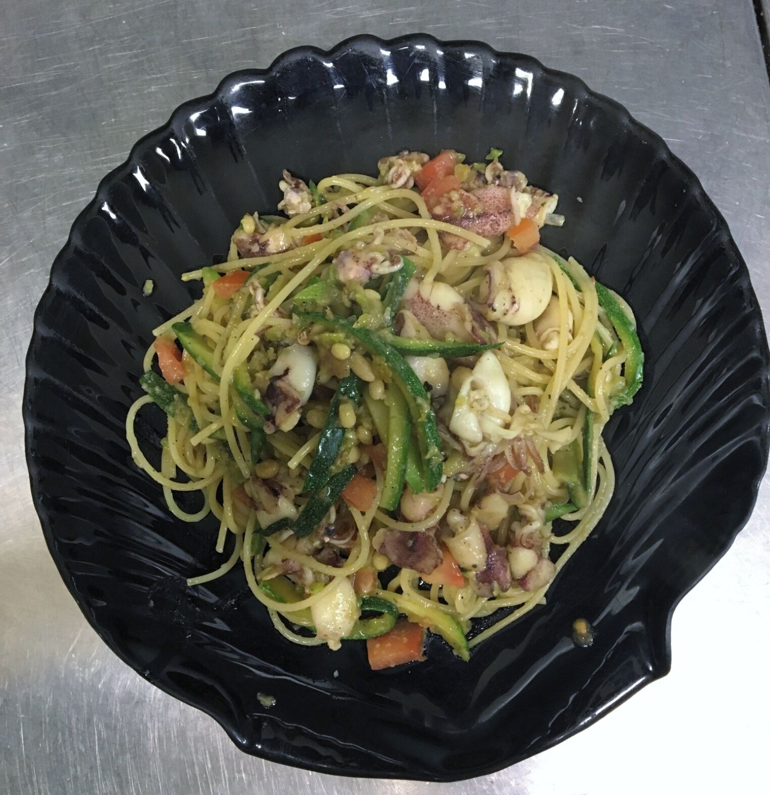 A black plate with a pasta dish containing vegetables and meat.