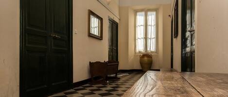 A hallway with a checkered floor, a wooden bench, and a large vase.