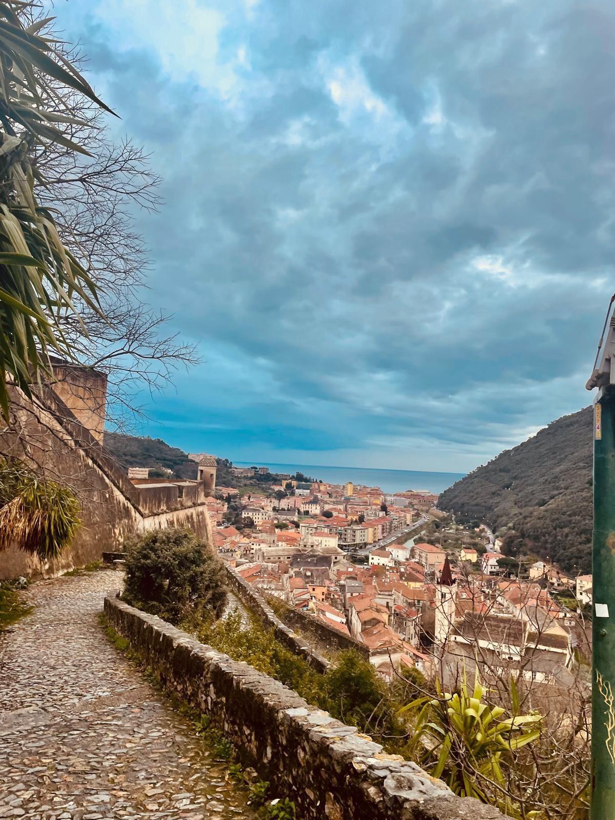 Un sentier pavé de pierres menant à une ville historique, caractérisée par ses murs de pierre et ses bâtiments à étages.