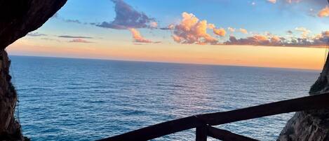 Vista desde la entrada de una cueva con vista al mar, y una barandilla de madera al frente.