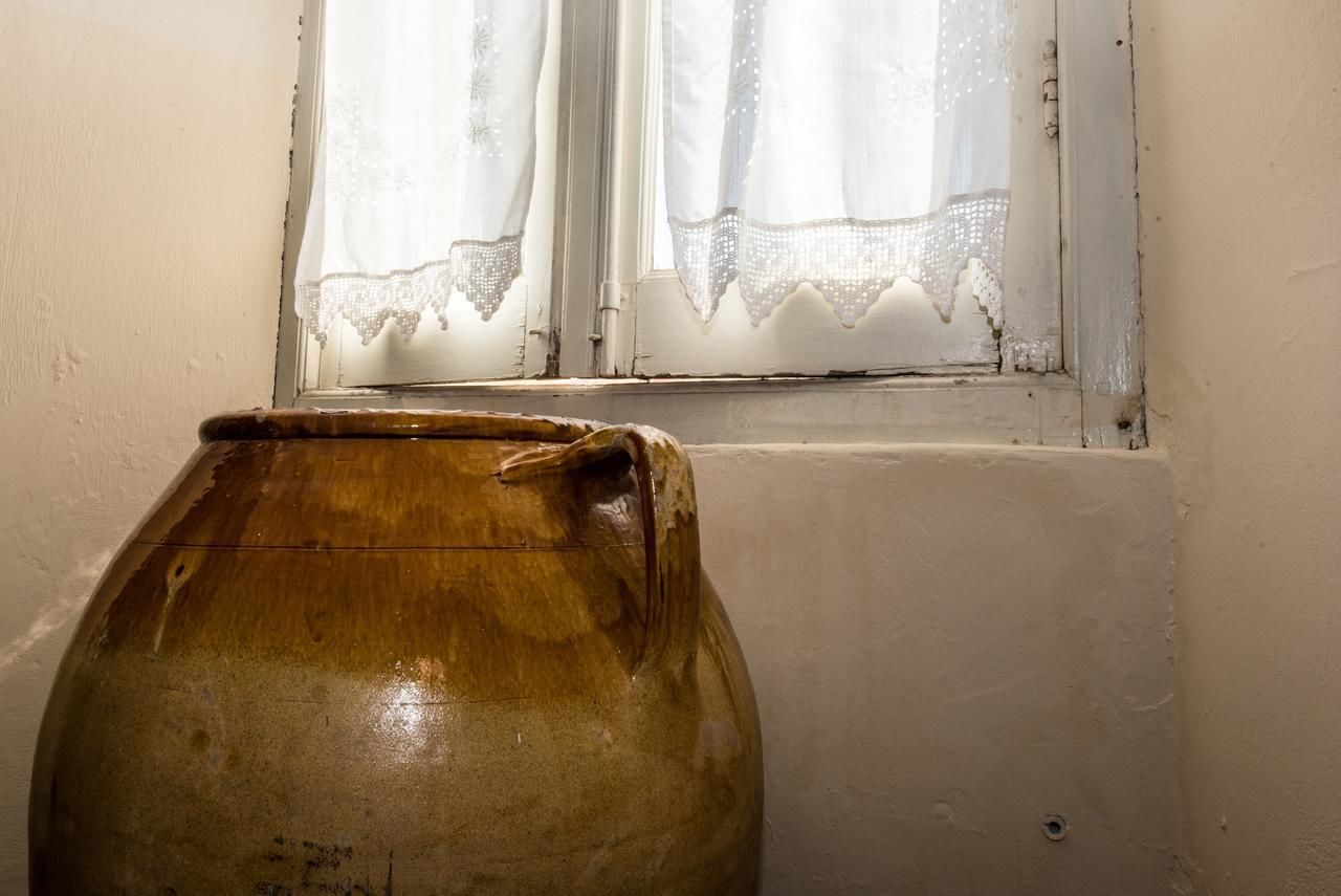 A large ceramic jug placed near a window with lace curtains.