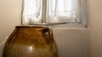 A large ceramic jug placed near a window with lace curtains.