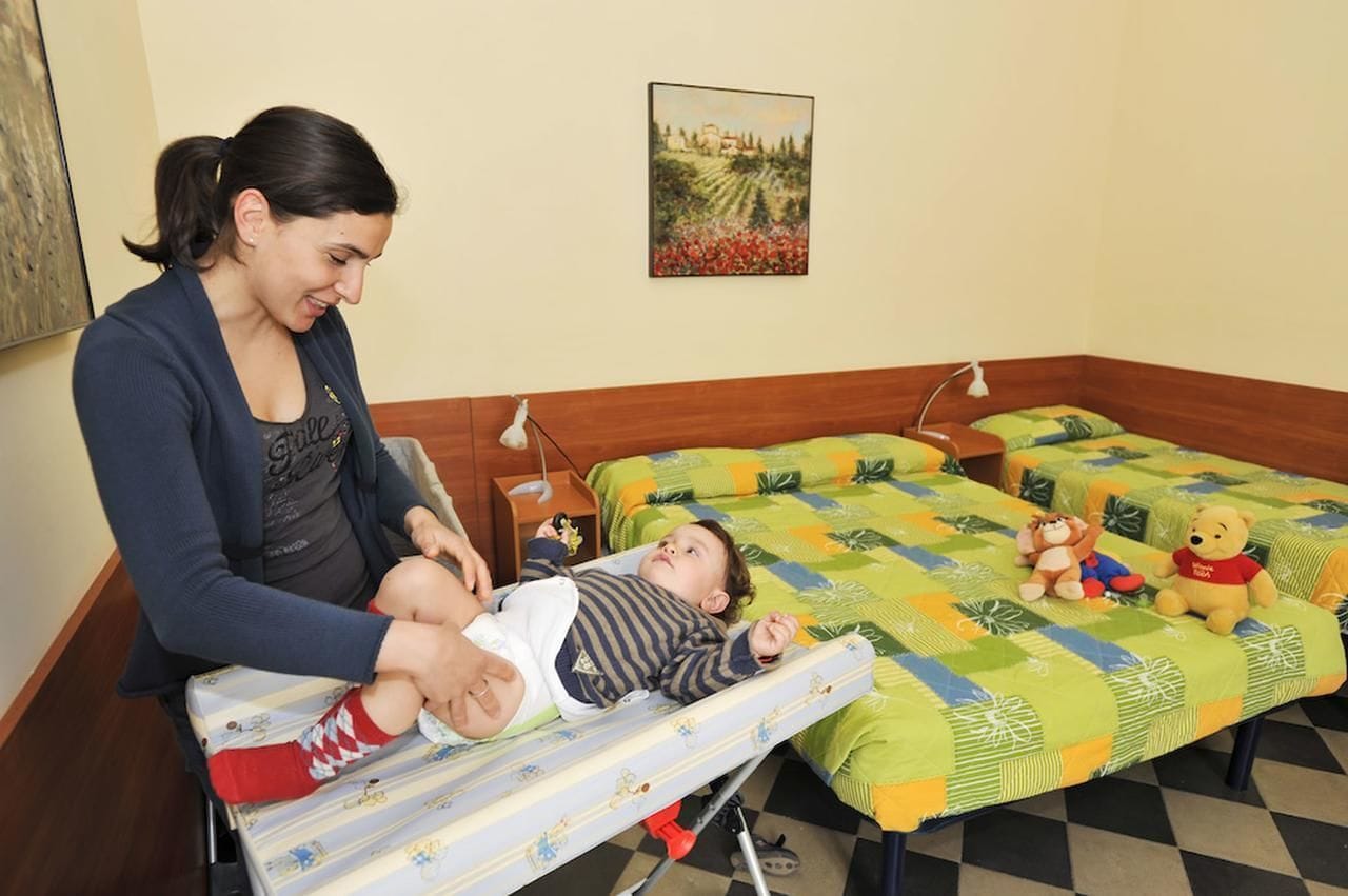 Una habitación con una cama, una cuna y una mesita de noche con lámpara.