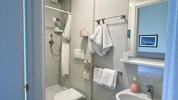 A modern bathroom with a toilet, bidet, and sink. There are towels hanging on a rack, a soap dispenser, and a picture on the wall.