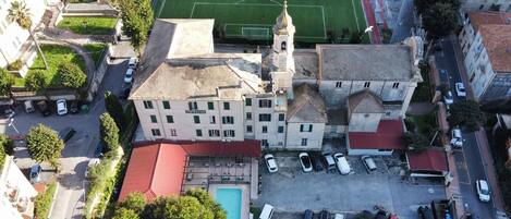 Vista aérea de un edificio con piscina, varias plazas de estacionamiento y un campo deportivo.