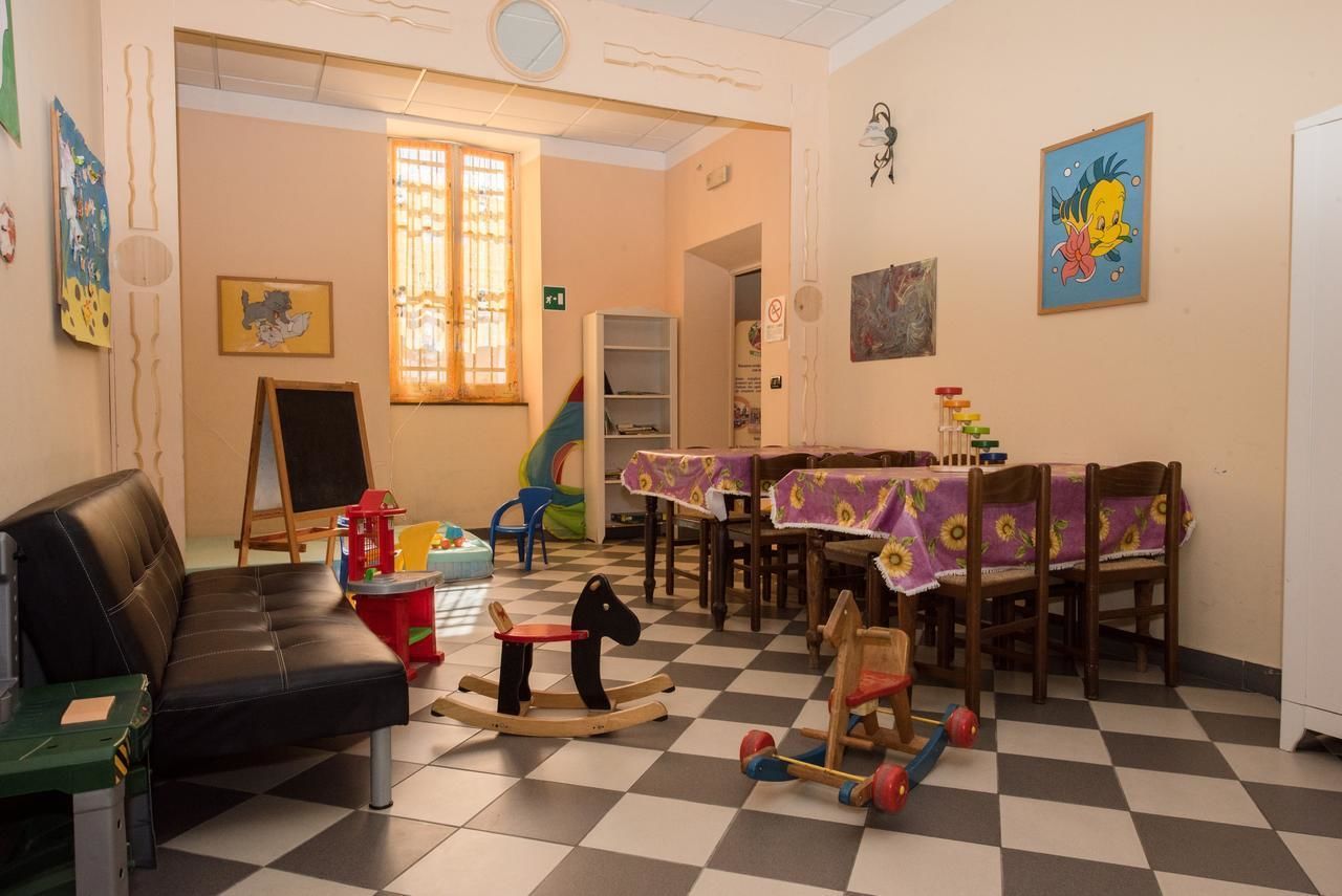 A room with a black leather sofa, a wooden rocking horse, a table with a floral tablecloth, and a window with bars.
