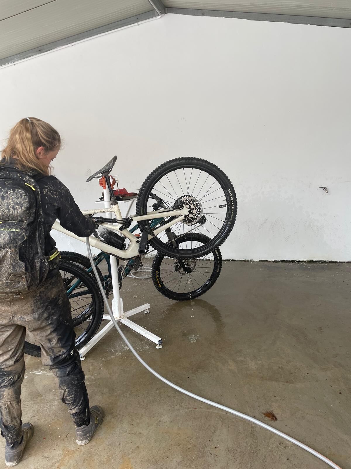 A person working on a bicycle in a garage with a concrete floor and white walls.