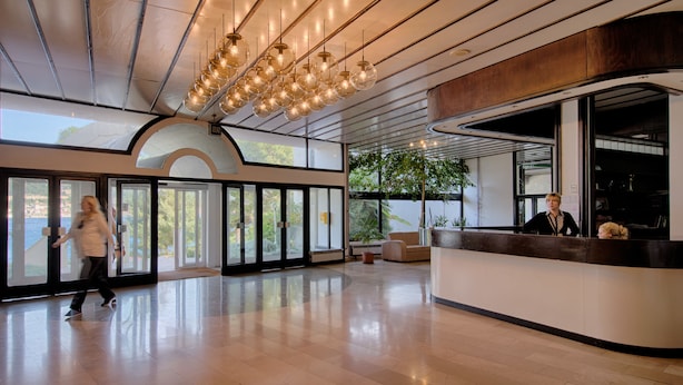 A spacious lobby with a reception desk, large windows, and a modern chandelier. - Hotel Issa (Vis)