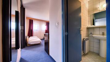 A hotel room with a bed, a desk, and a bathroom with a sink and radiator.