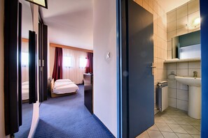 A hotel room with a bed, a desk, and a bathroom with a sink and radiator.