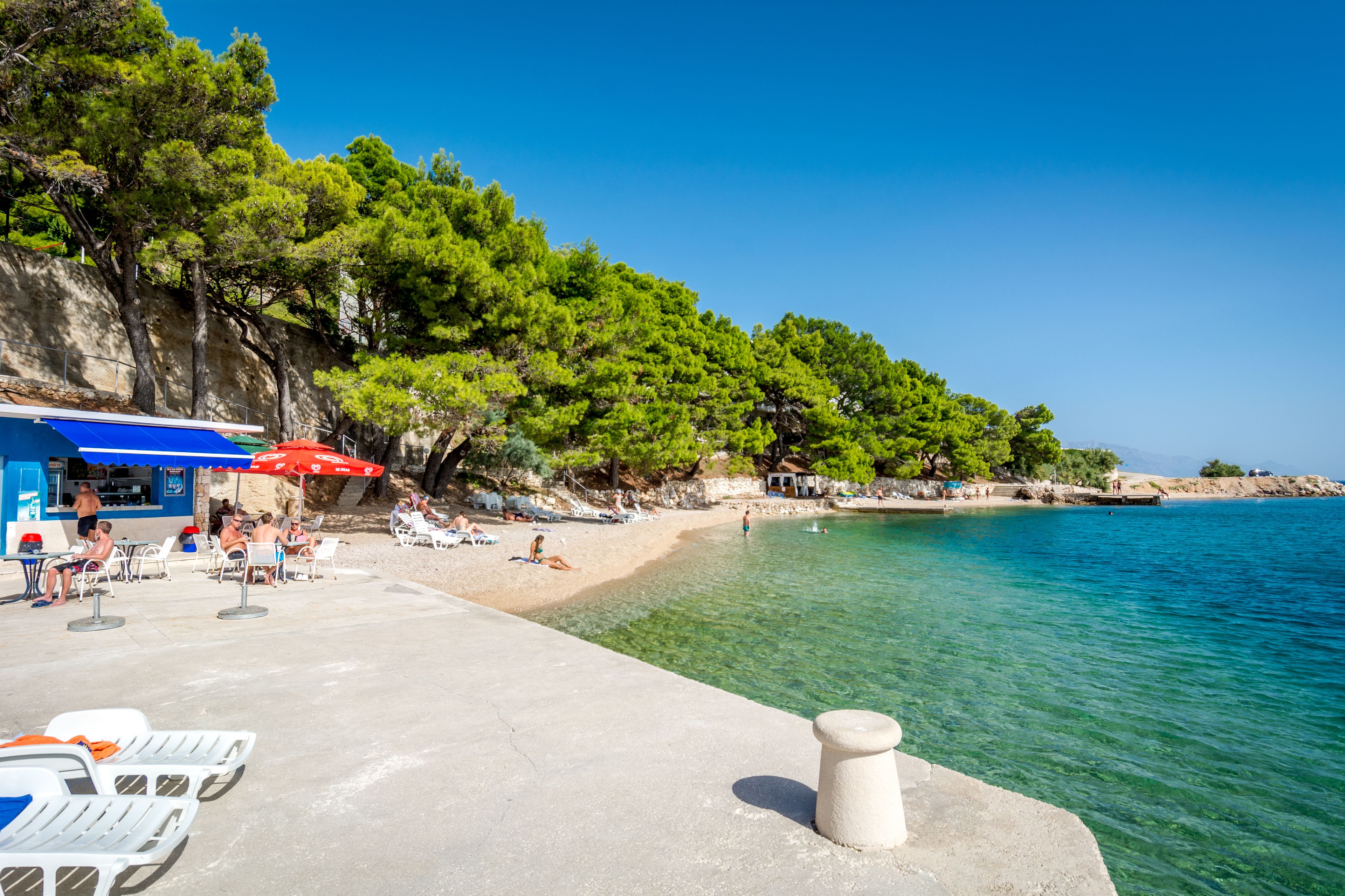 A beach with clear turquoise water, white lounge chairs, and umbrellas.