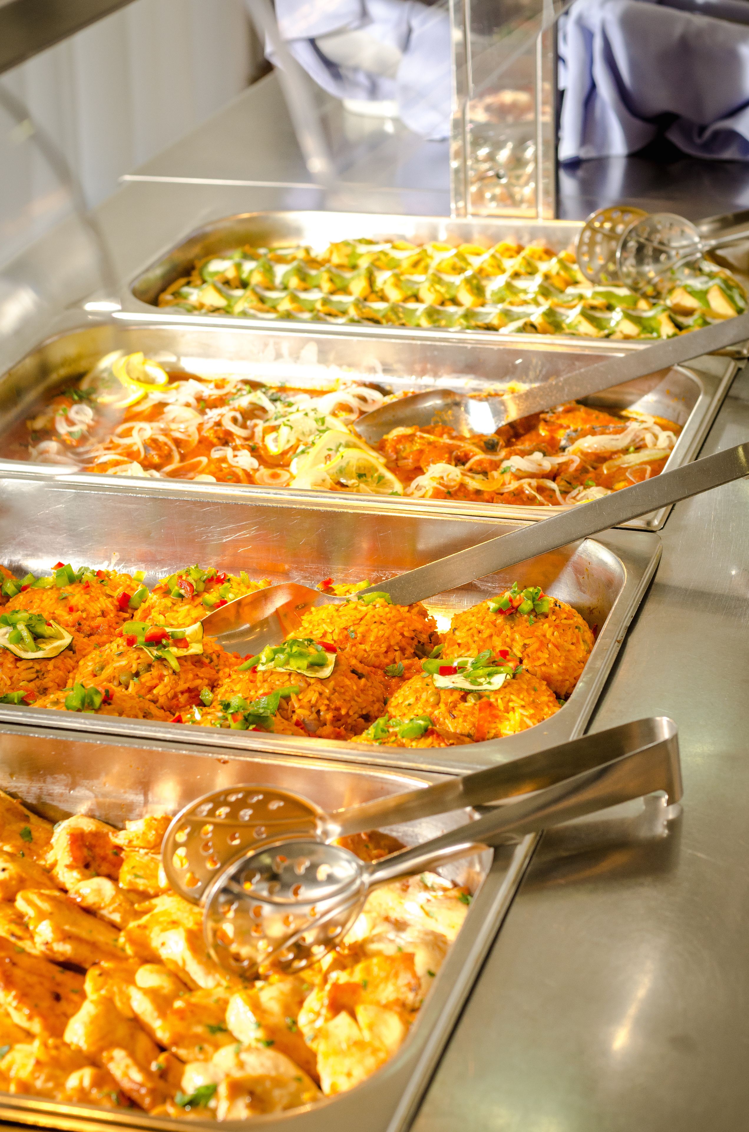 Monipuolinen buffet, jossa on tarjolla erilaisia ruokia, kuten riisiä, kanaa ja kasviksia.