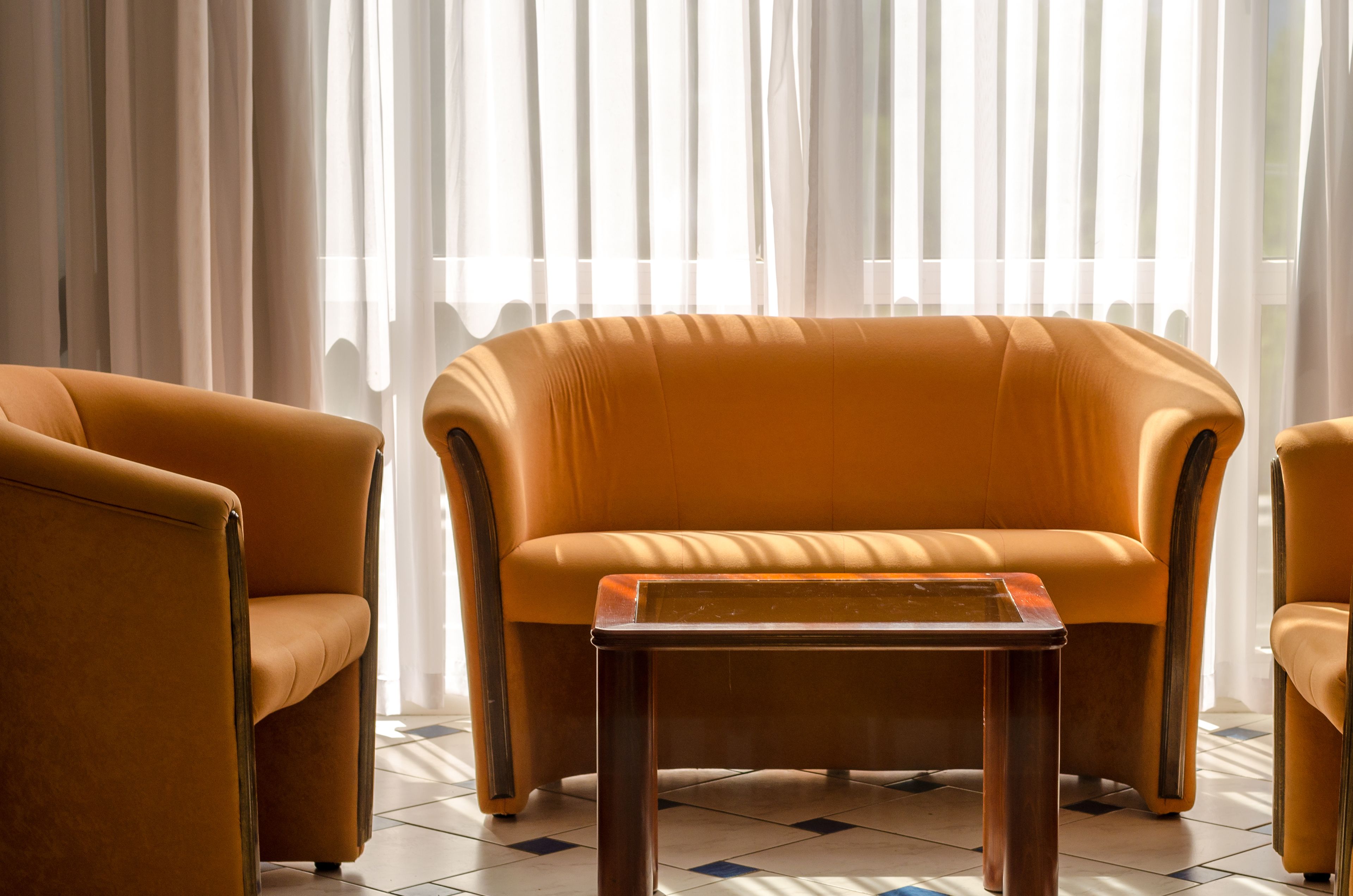 A living room with a sofa and two armchairs, a coffee table, and a large window with sheer curtains.