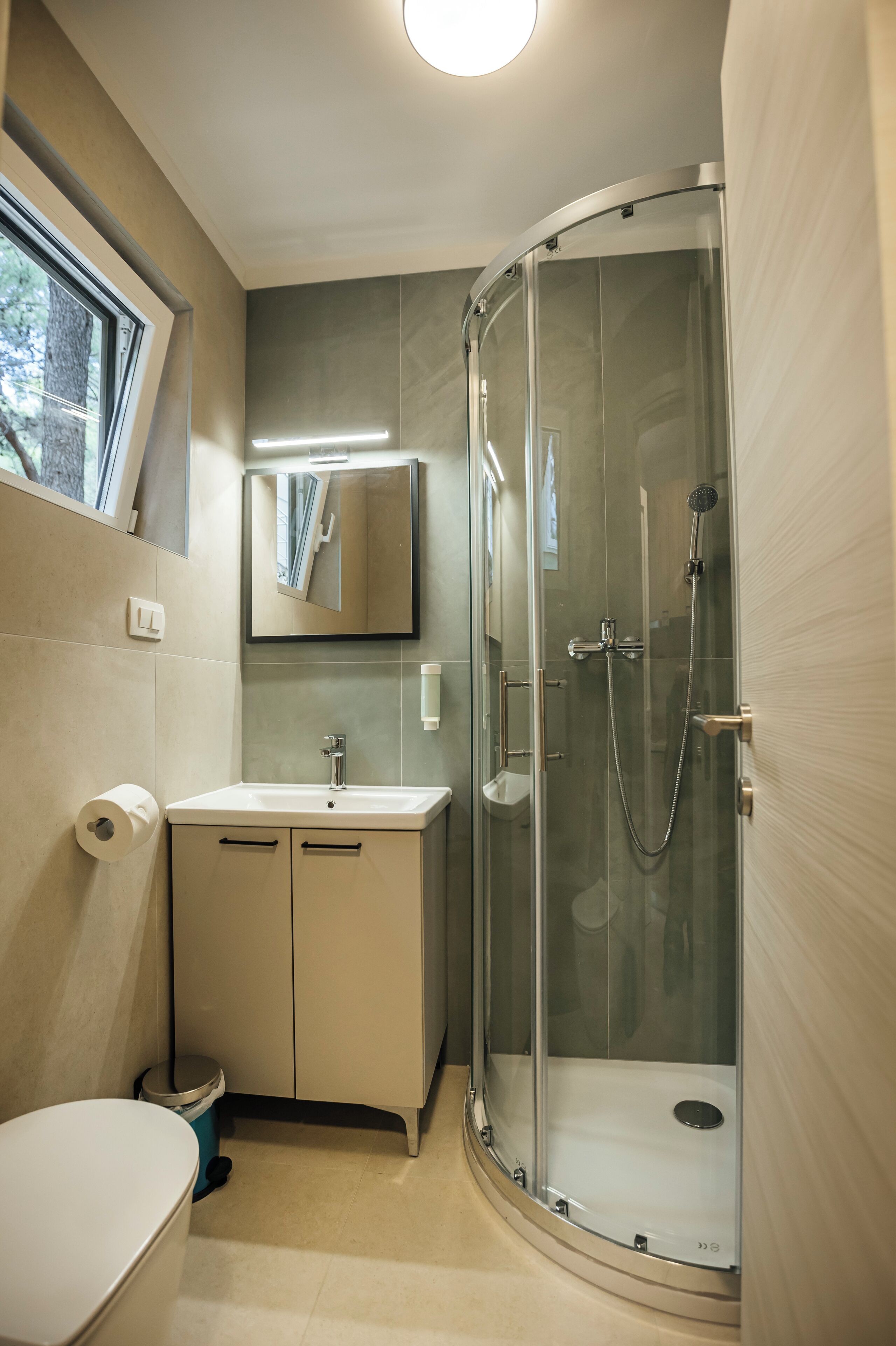 Een moderne badkamer met een douchecabine van glas, een wastafel met spiegel erboven en een toilet.