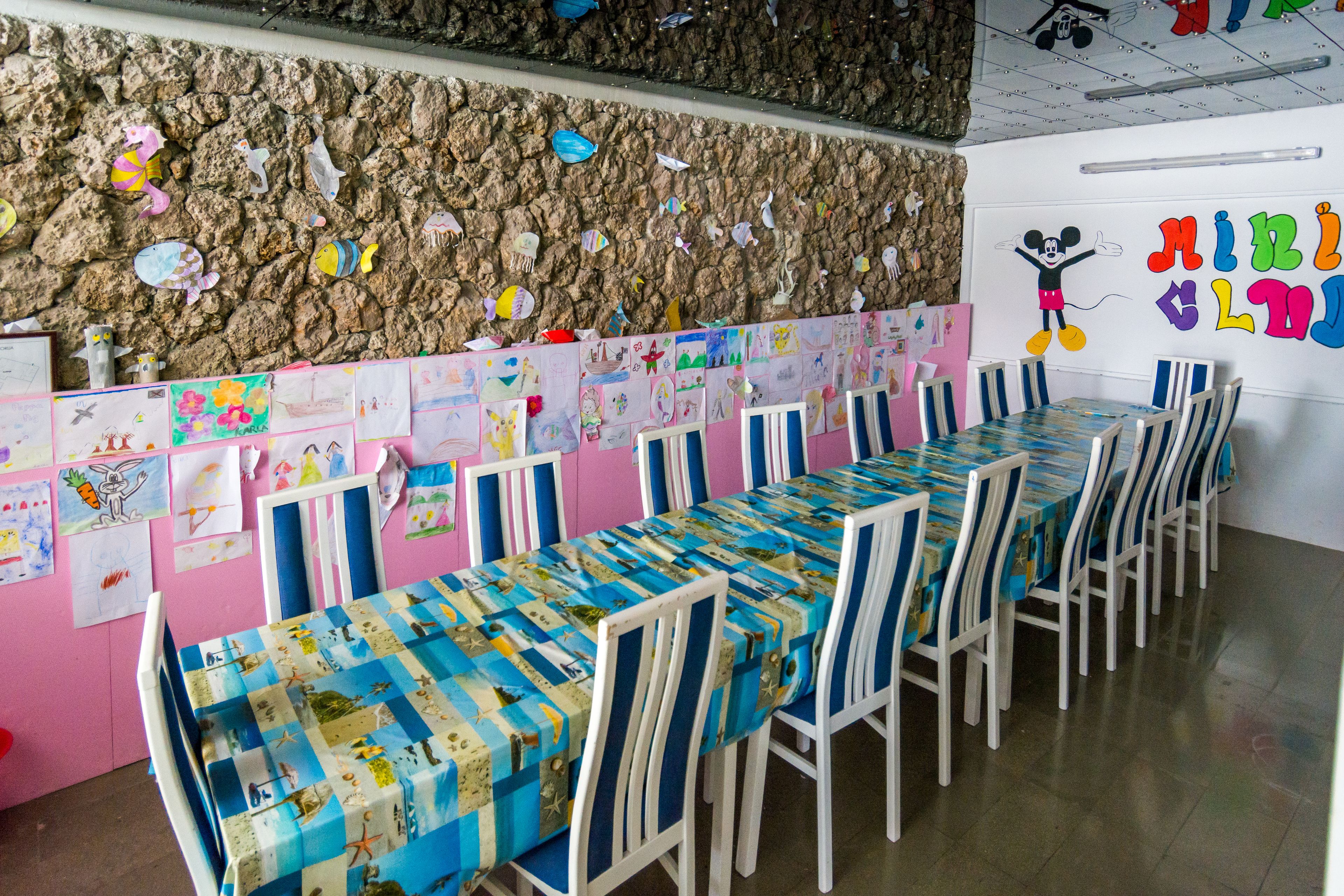 A long dining table with chairs, a wall with children's drawings, and a Mickey Mouse mural.