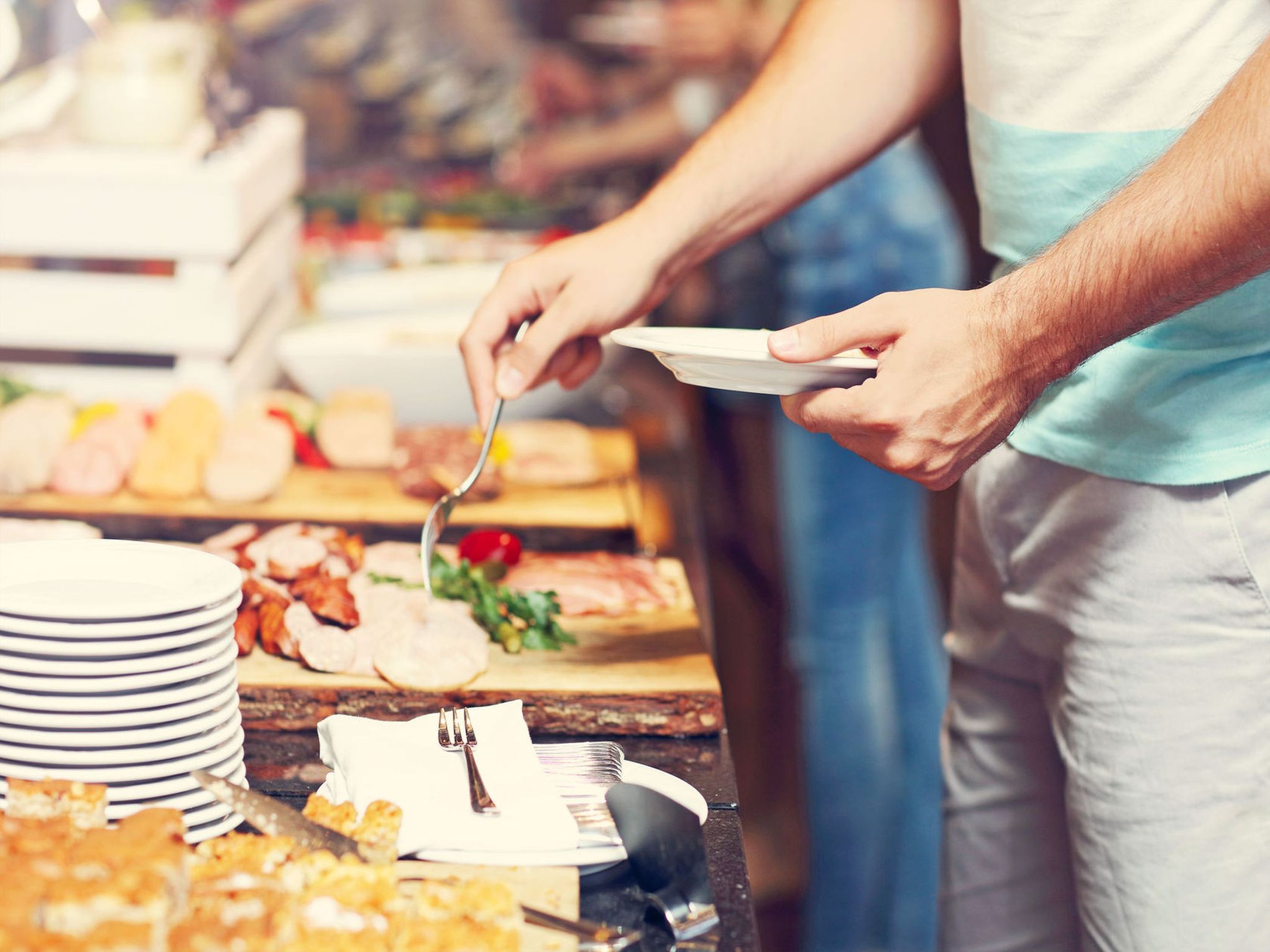 Montaje de bufé con diversos alimentos y una persona sirviéndose.