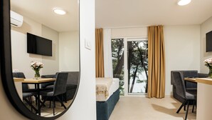 A modern hotel room with a bed, a desk, a chair, a TV, and a view of trees through the window. - Sagitta all inclusive holiday resort (Omis)